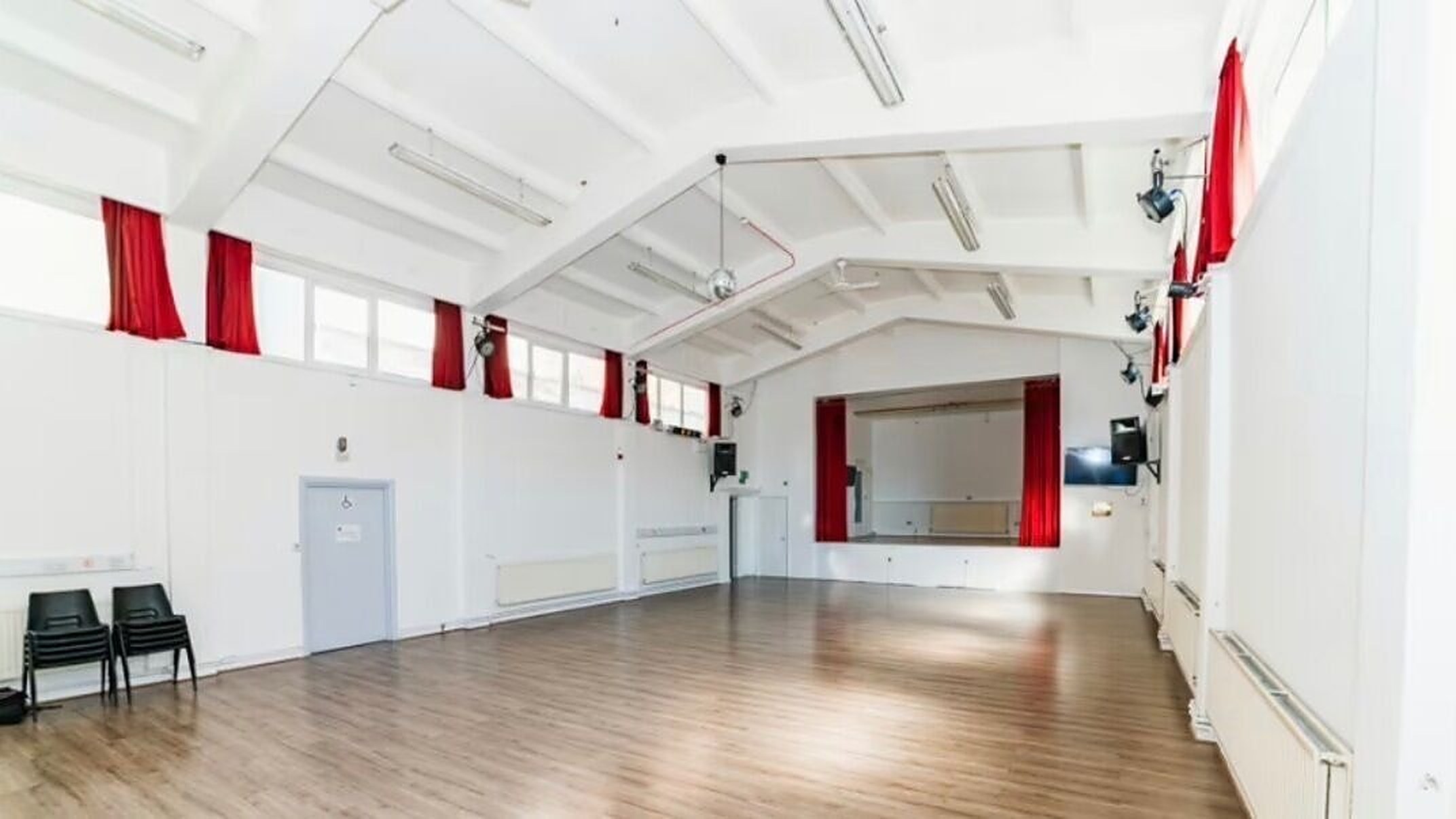 The main hall at Themixer.uk, with a wooden floor and deep red stage curtains
